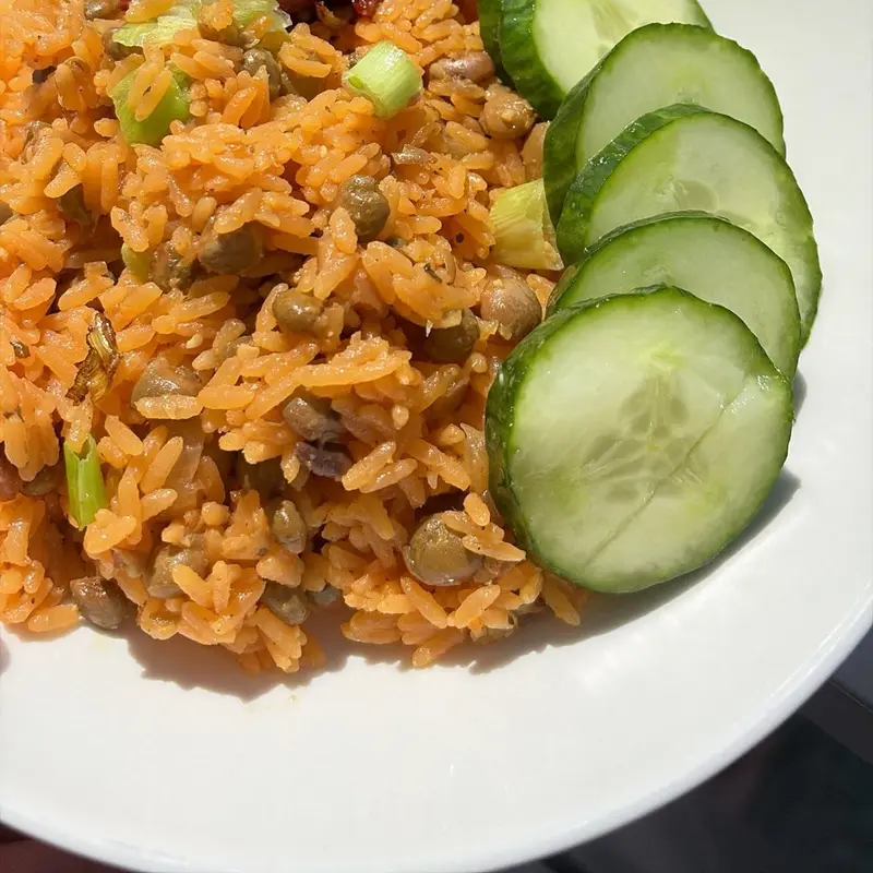 Rice with pigeon peas and sausage, with sliced cucumber on the side.